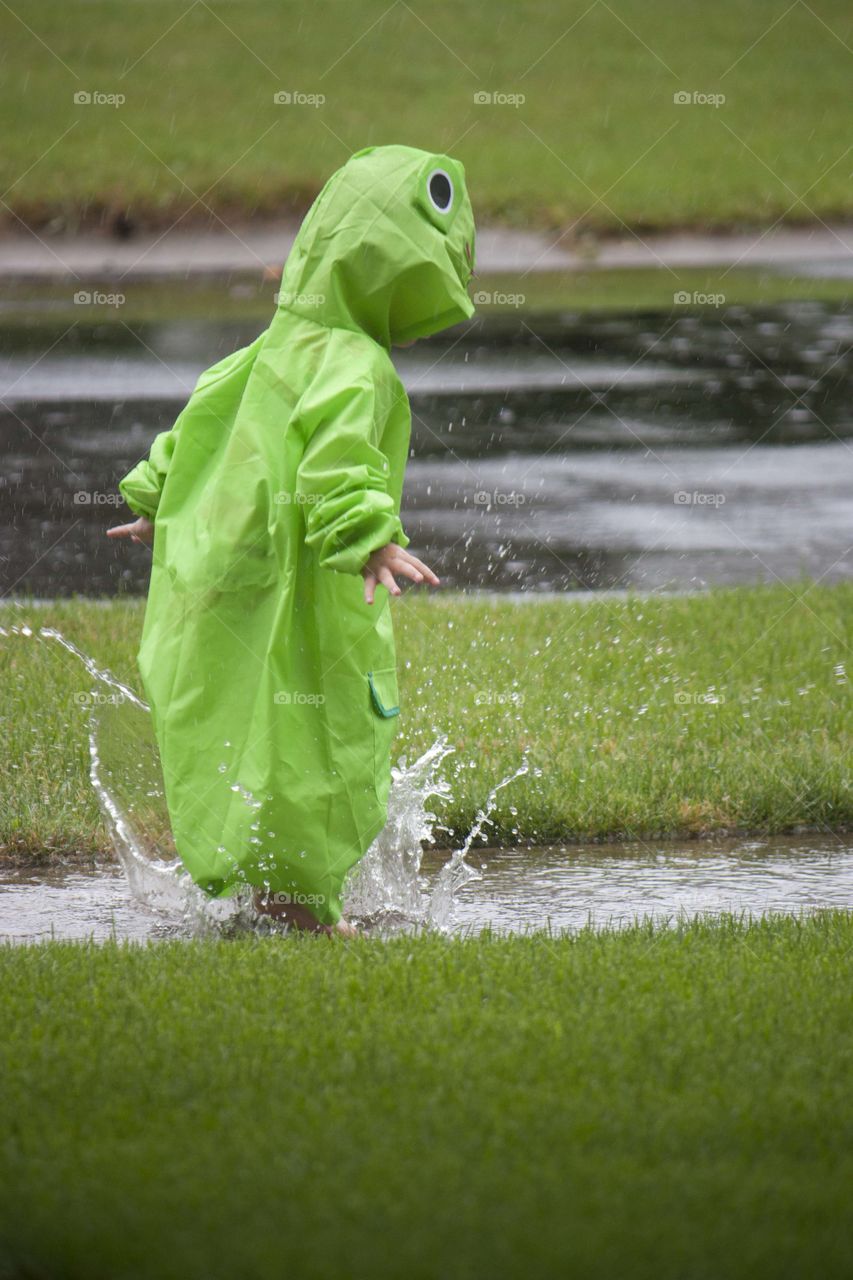 Boy wearing raincoat and splashing in puddle