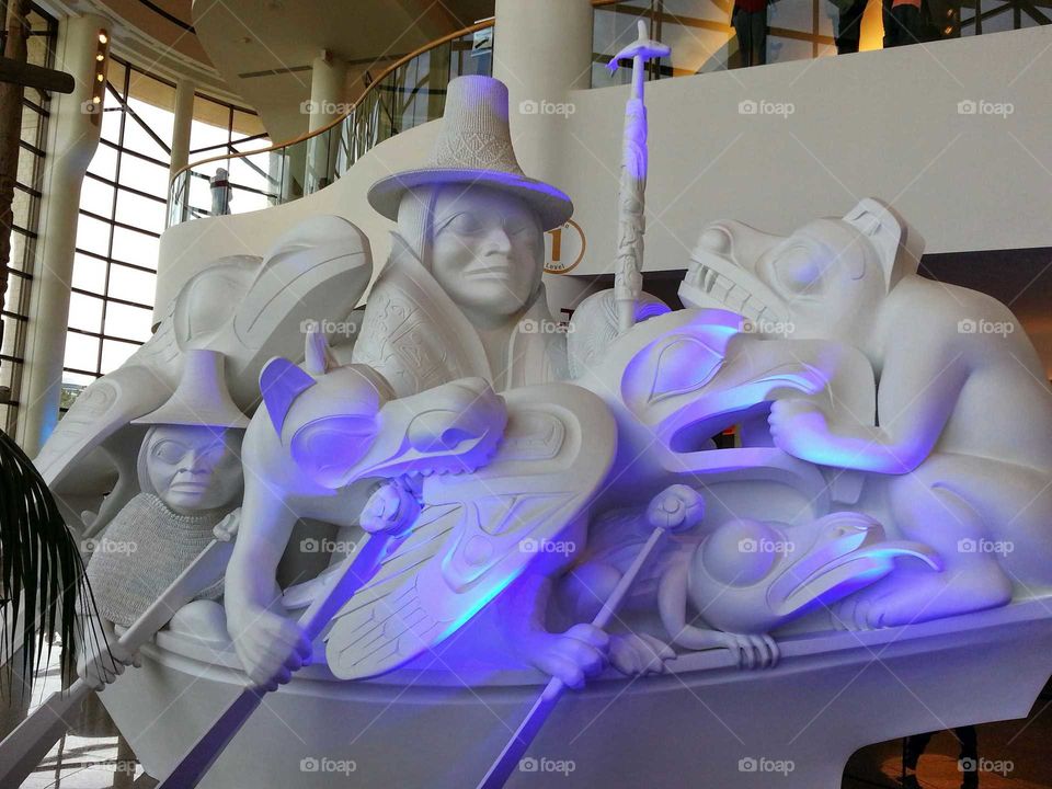 A big sculpture showing people and animals from the first nations on a canoe  with purple lighting at the National Museum of the American Indian