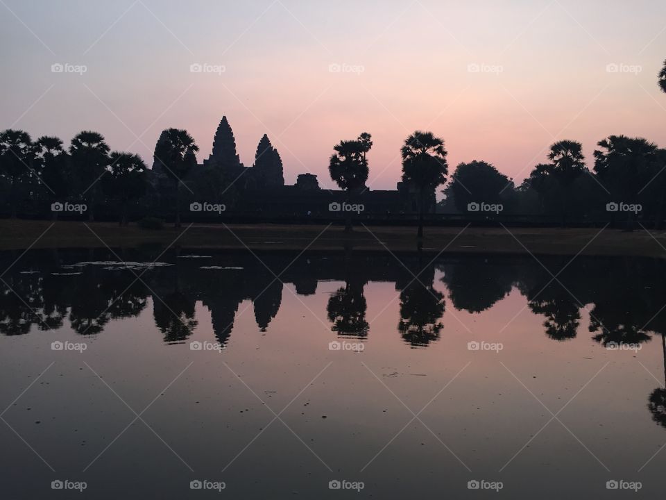 Angkor Wat temple in Cambodia at sunrise. Offset picture with water reflection. Silhouette of temple shown.