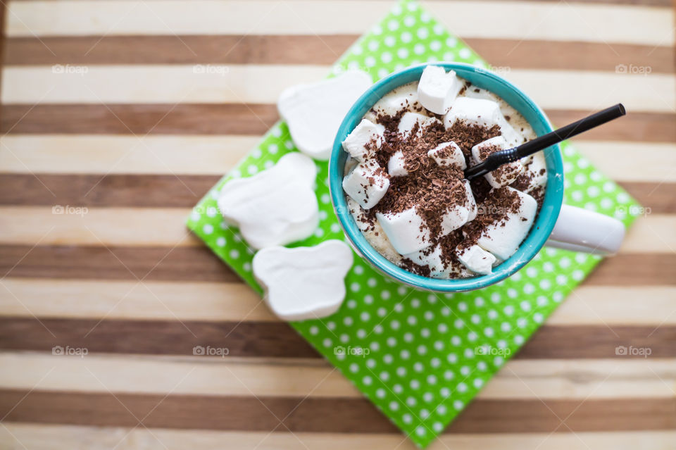 A cup of coffee with marshmallows sprinkled with chocolate chips and a black straw, stands on a tray and a green napkin