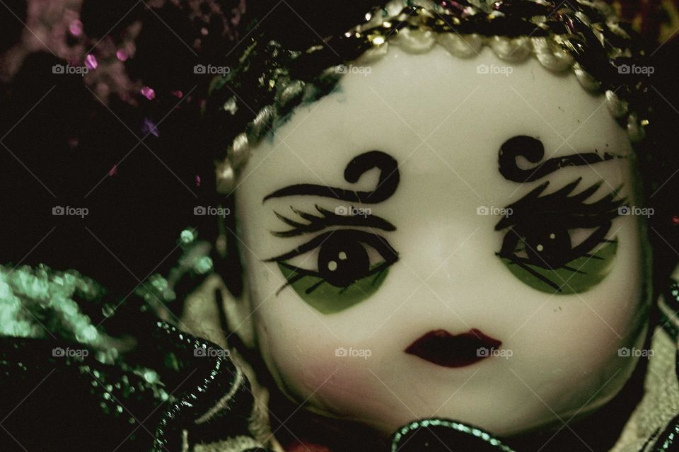 Closeup of the face of a vintage Venetian porcelain doll dressed as a Jester in traditional Carnival colours of amethyst and emerald. 