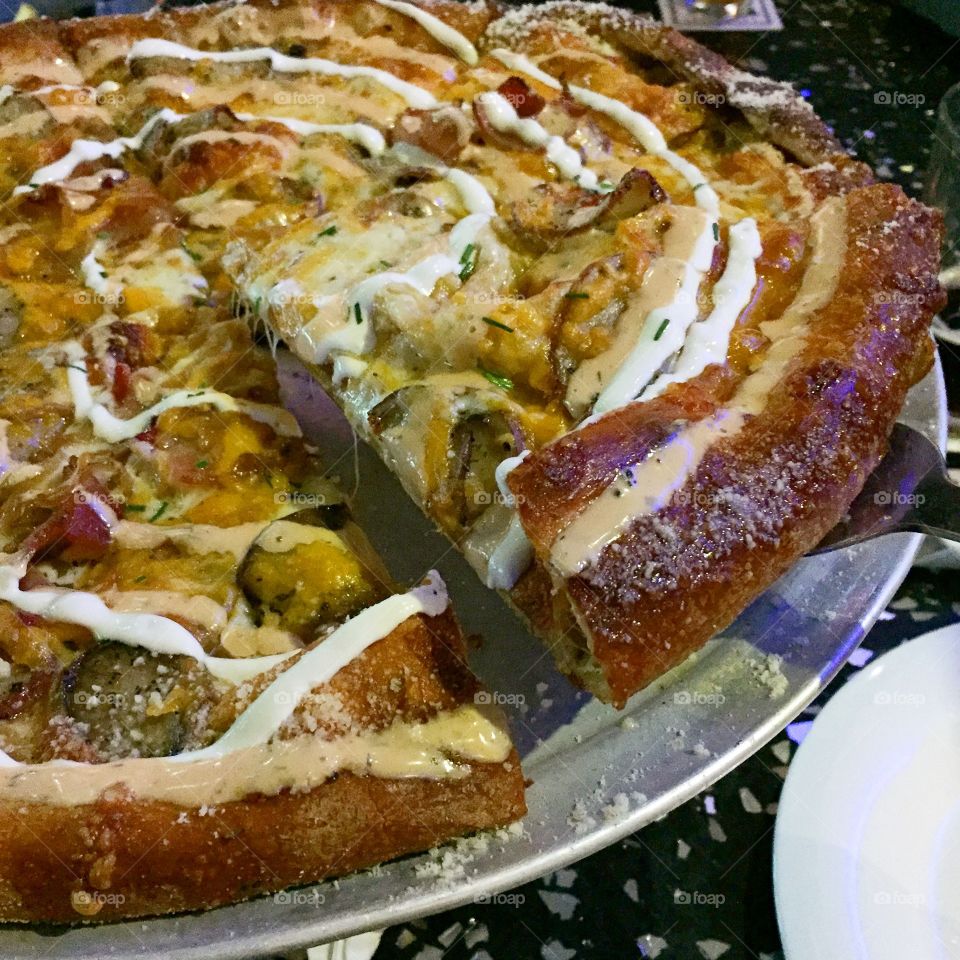 A brick oven baked pizza with red potatoes, bacon, onions and more topped with sour cream and spicy ranch dressing 