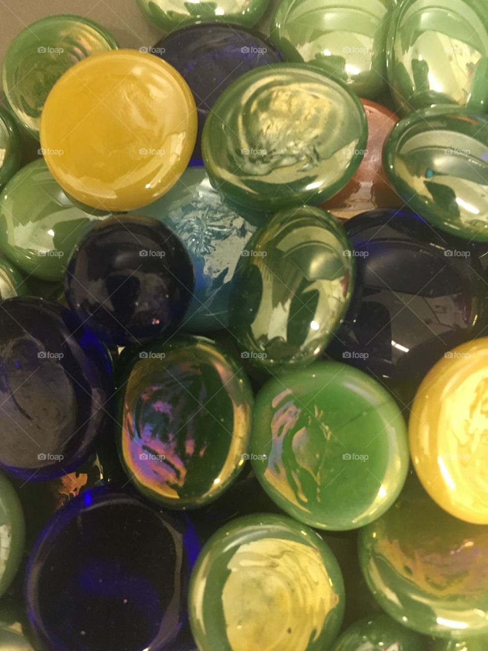 Glass Beads-A close up view of round glass beads in greens, yellows, and blues.  the beads are shiny, bright, and circles.