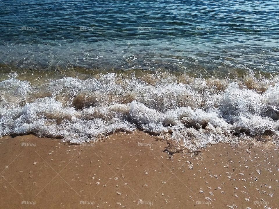 a beautiful turquoise wave rolling in towards the sand shore on sunny fall afternoon