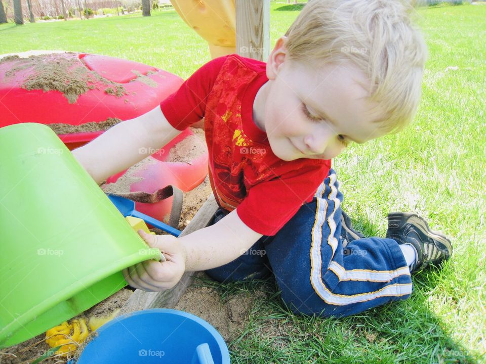 Darling photo of young boy holding his green sand bucket playing in the sand box!! 