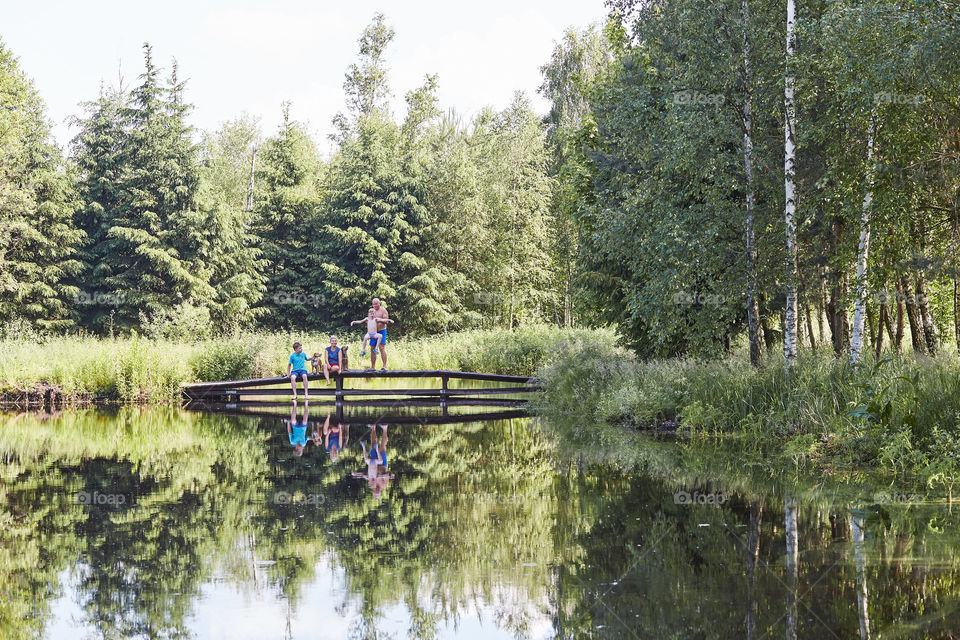 Family spending time together sitting on a bridge over a lake, among the trees, close to nature, during summer vacations. Candid people, real moments, authentic situations