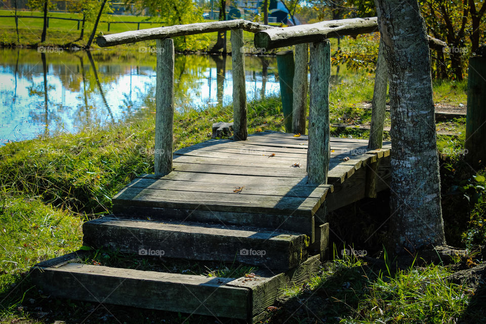 A small wooden bridge at the trailhead of a path around a small lake in the summer. 