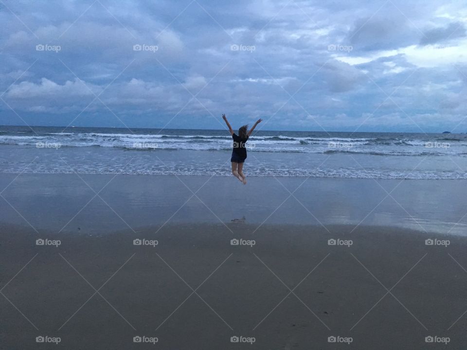 Garota de costas pulando de felicidade na areia da praia. Mar e céu azuis
