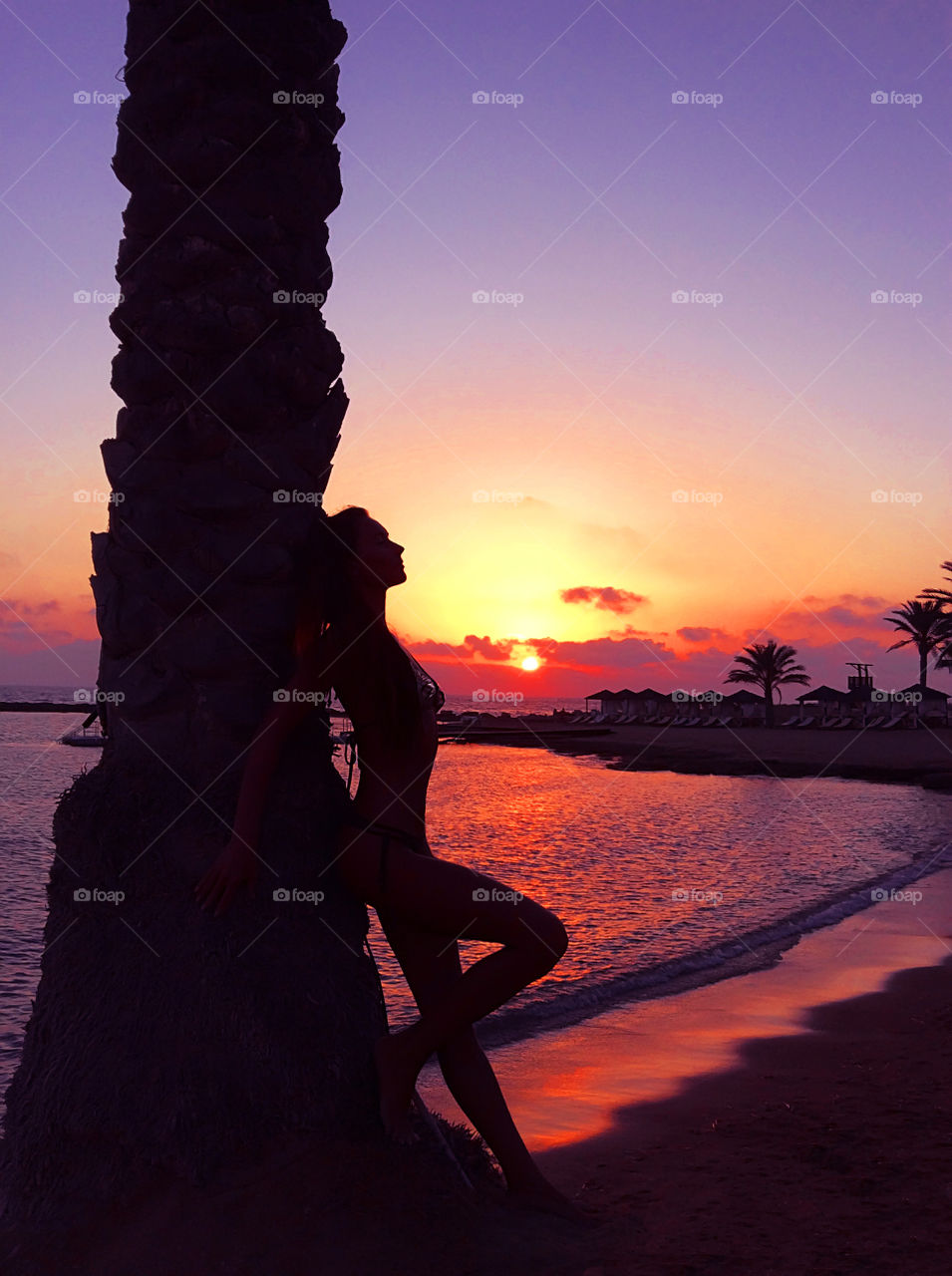 Silhouette of a young woman at the palm tree on sunset at the beach background 