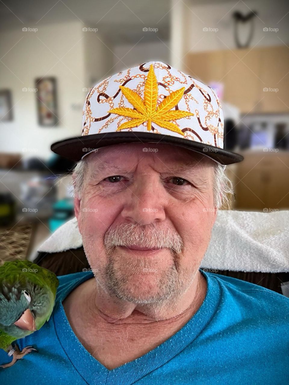 Man wearing a hat with his pet parrot on his shoulder.