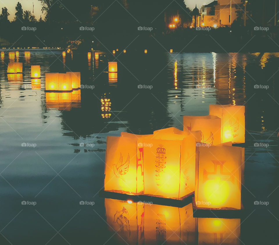 Bright orange lanterns float smoothly along the Rio Nabão in the late evening