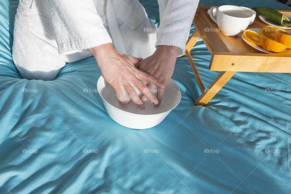 A man at home takes care of himself and does a manicure at home on a blue background and with orange.