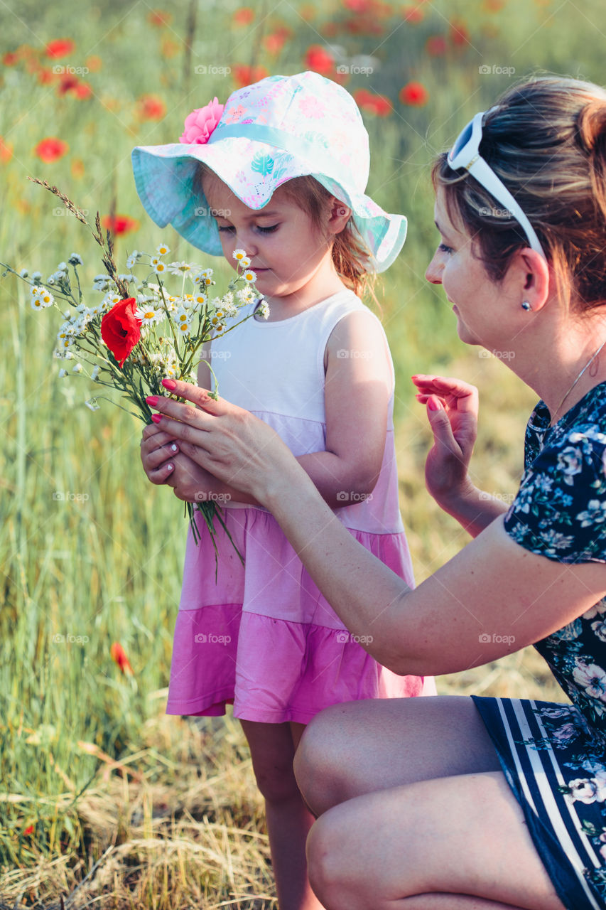 Mother and her little daughter in the field of wild flowers. Little girl picking the spring flowers for her mom for Mother's Day in the meadow. Girl handing the flowers to her mom. Nature scene, family time