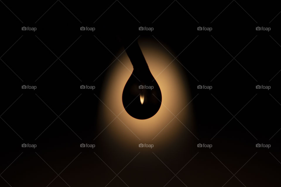 A macro portrait of the silhouette of a drop of water against the light of the flame of a candle. inside the silhouette of the droplet the flame is visible upside down because it is refracted in the water.