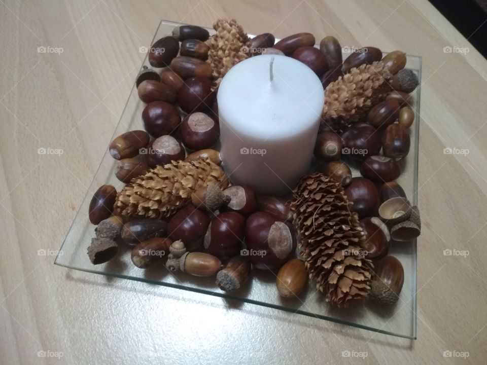 white candle with decorative brown pine cones, horse chestnuts and acorns