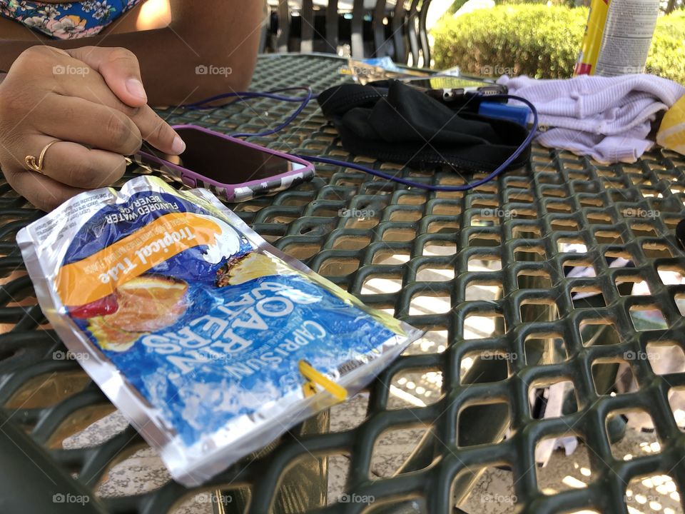 An empty Roarin’ Waters Capri Sun laying on a table, next to a girl on her phone