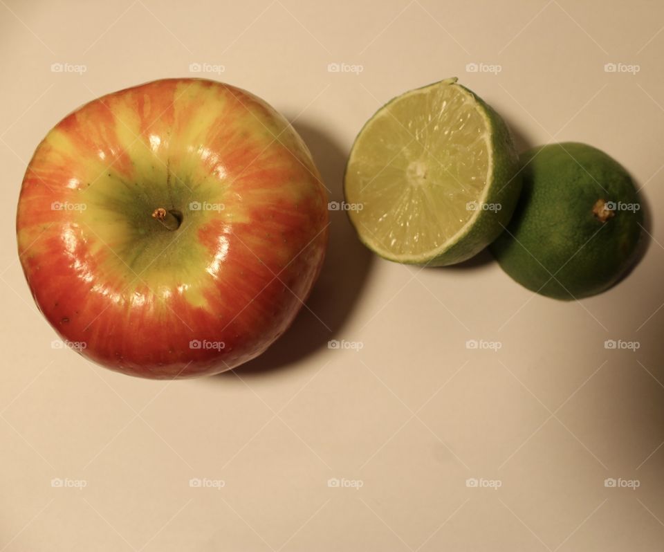 Two fruits including an apple and a sliced like on a clear white background with an overhead light source 
