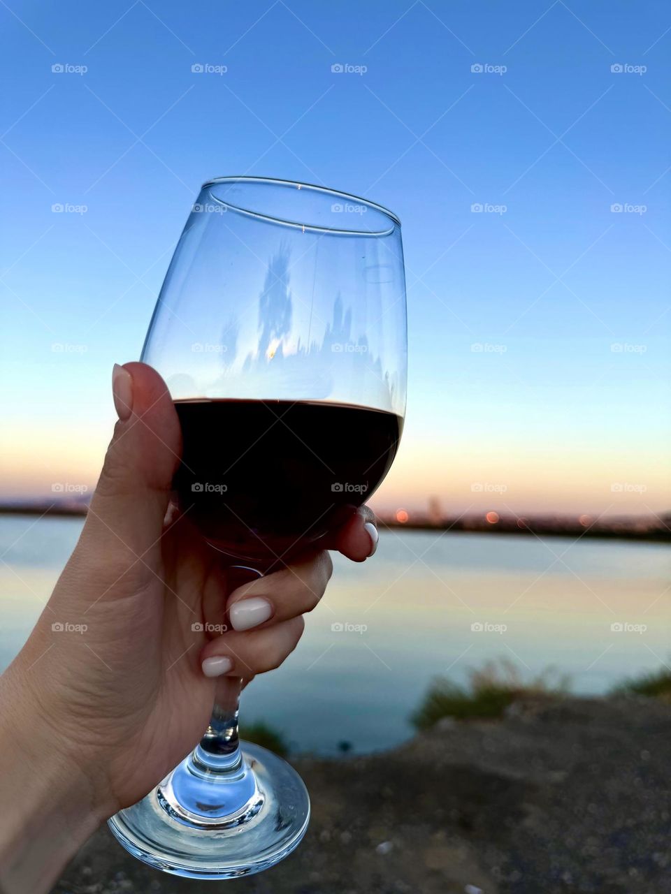 Glass of red wine in a woman's hand against the backdrop of the sea