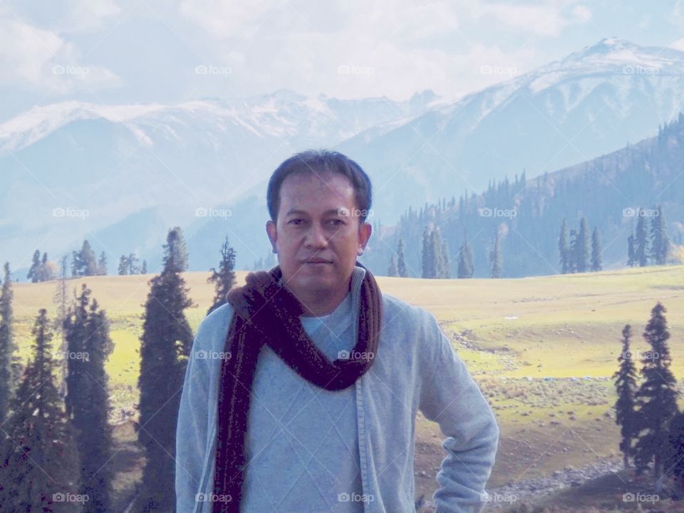 Man with cozy sweater against mountain range and blue sky background 