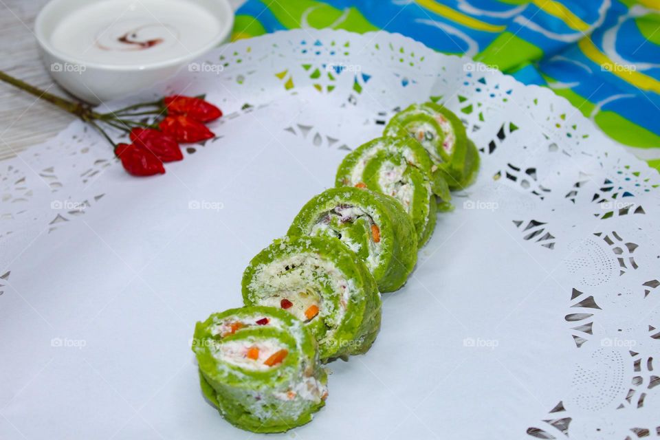 Rolled spinach pancakes filled with cream cheese and vegetables on a white background