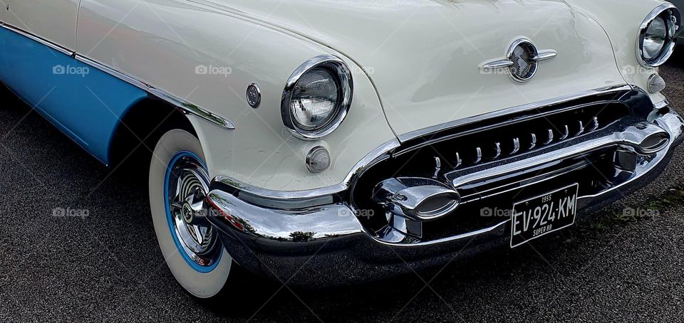 The front lights, grill and tyre of a blue and cream Oldsmobile 88 car at Cherbourg car show