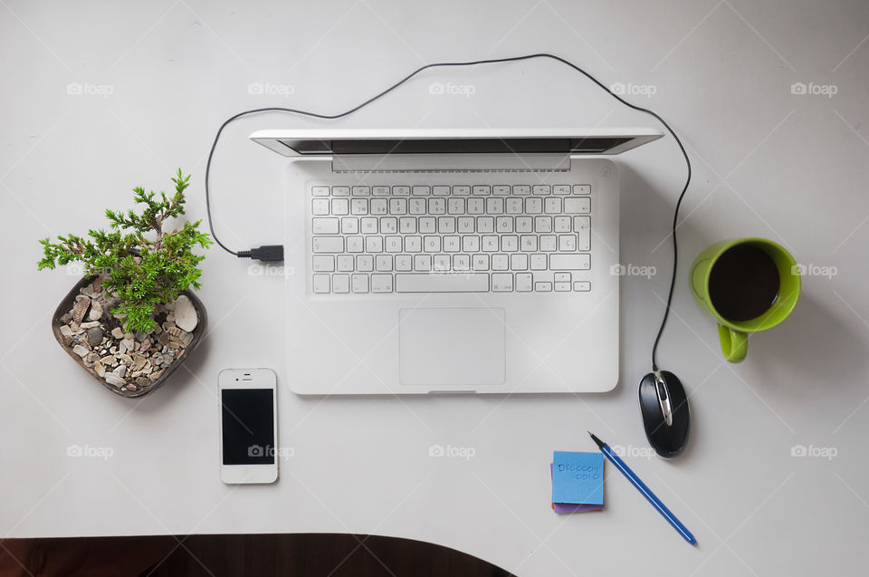 White laptop with a black wired mouse on a whites desk and a white cellphone 