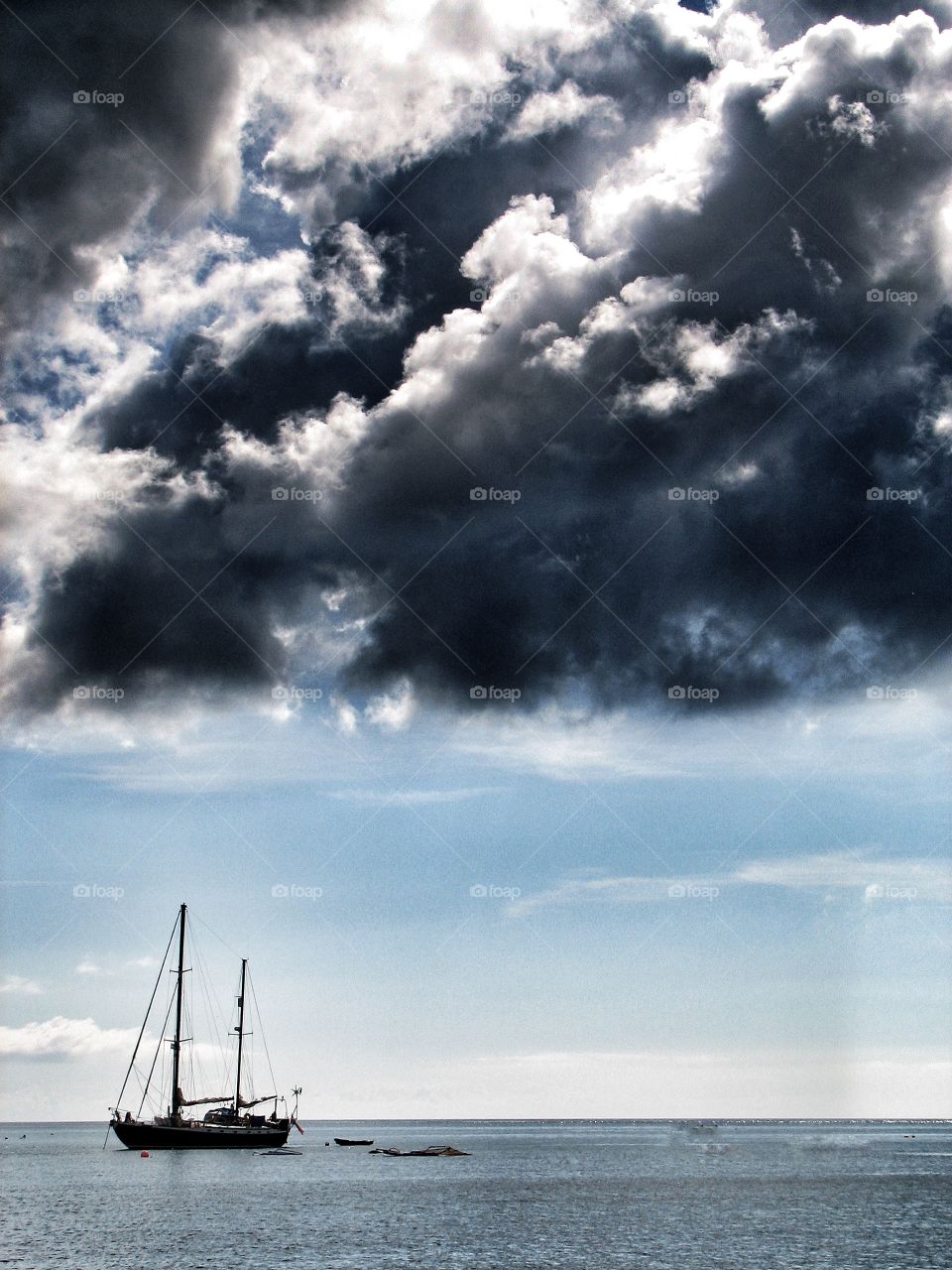 A black stormy cloud brewing above a single yacht floating on a calm sea.