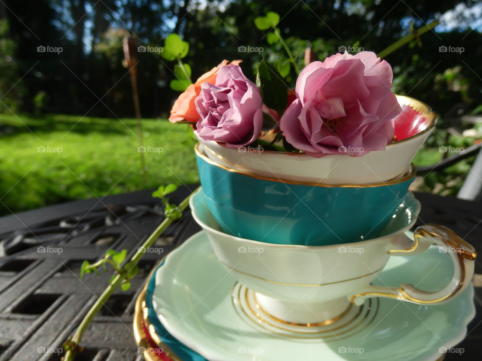 Garden tea party stack of vintage tea cups and saucers with tea roses conceptual background 