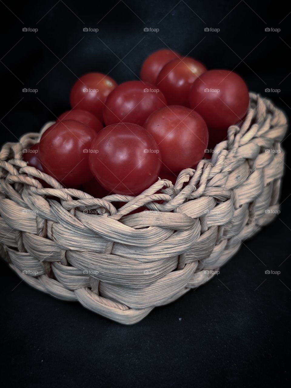 wicker wooden basket with cherry tomatoes on a black background.  side view