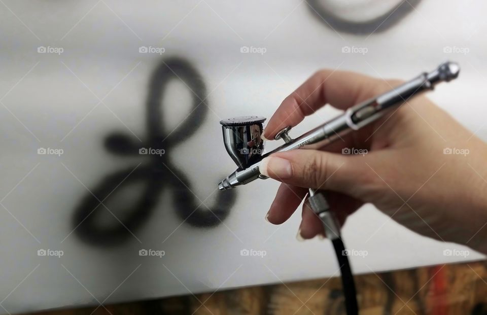 A woman learning how to use an airbrush to paint working on letters