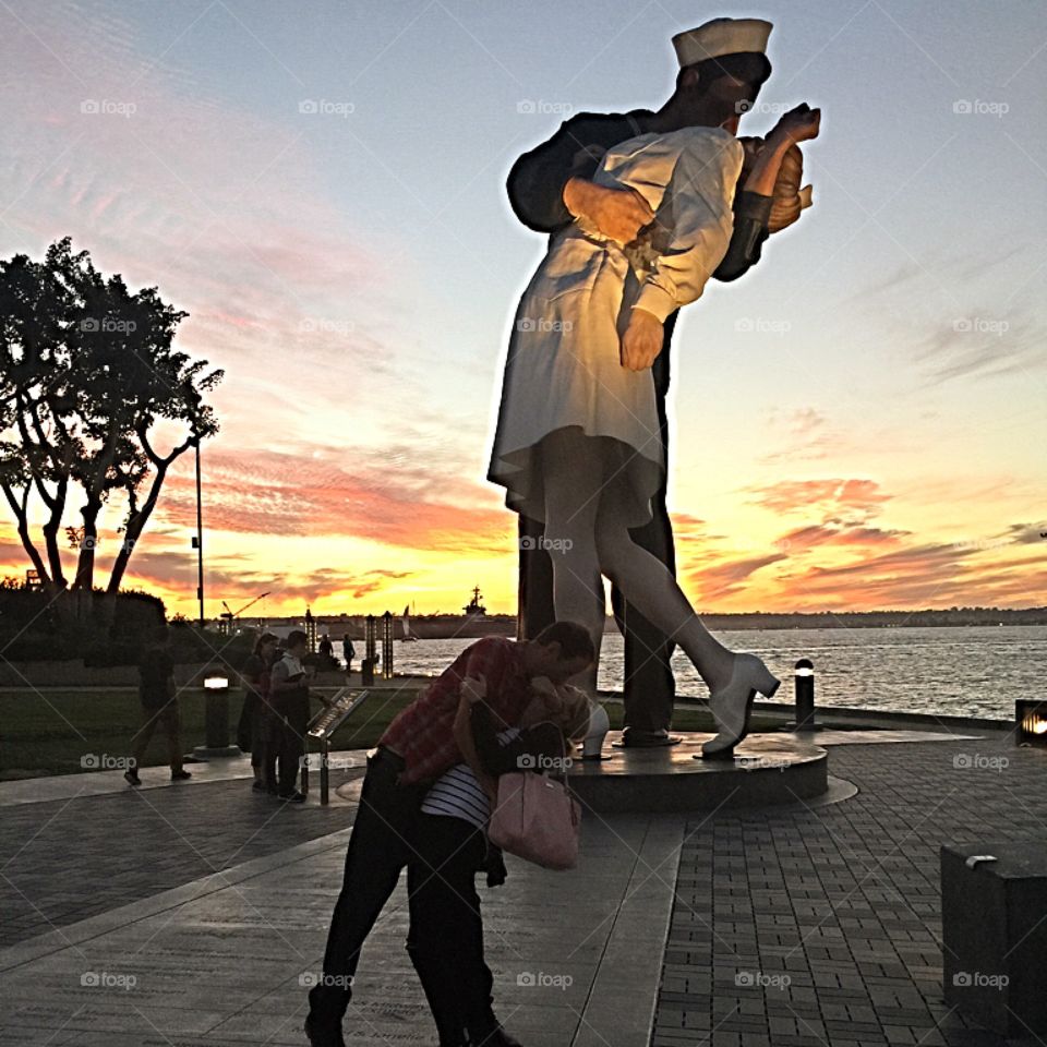 Two kissing lovers embraced in front of statue of a navy sailor and a nurse.  