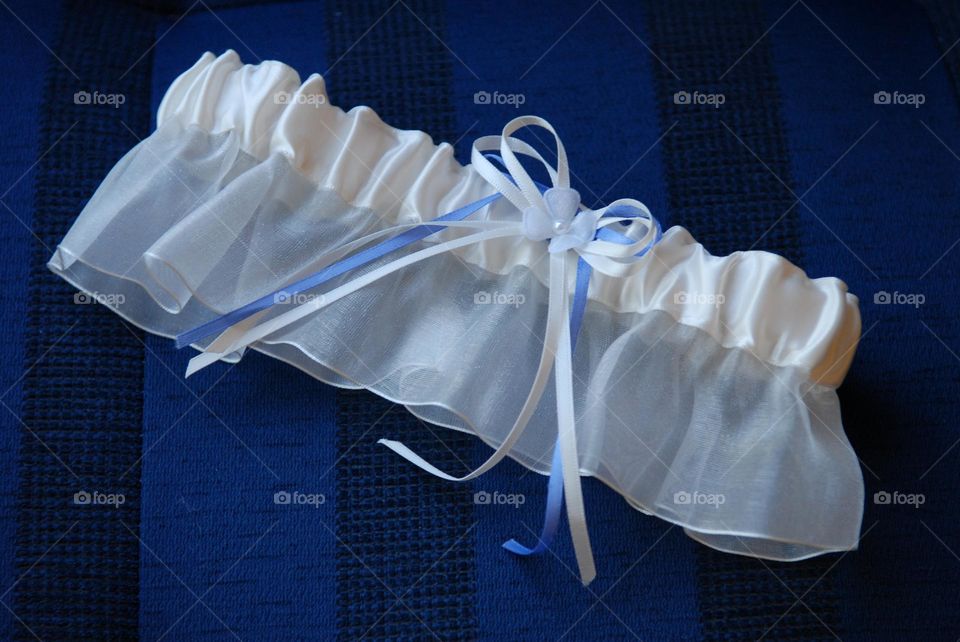 A detailed view of white garter with a baby blue and white ribbon tied in a bow against a dark blue background 