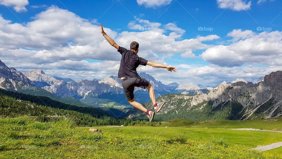 Happy young man jumping up in the air and clicking his heels in front of a magnificent mountain landscape