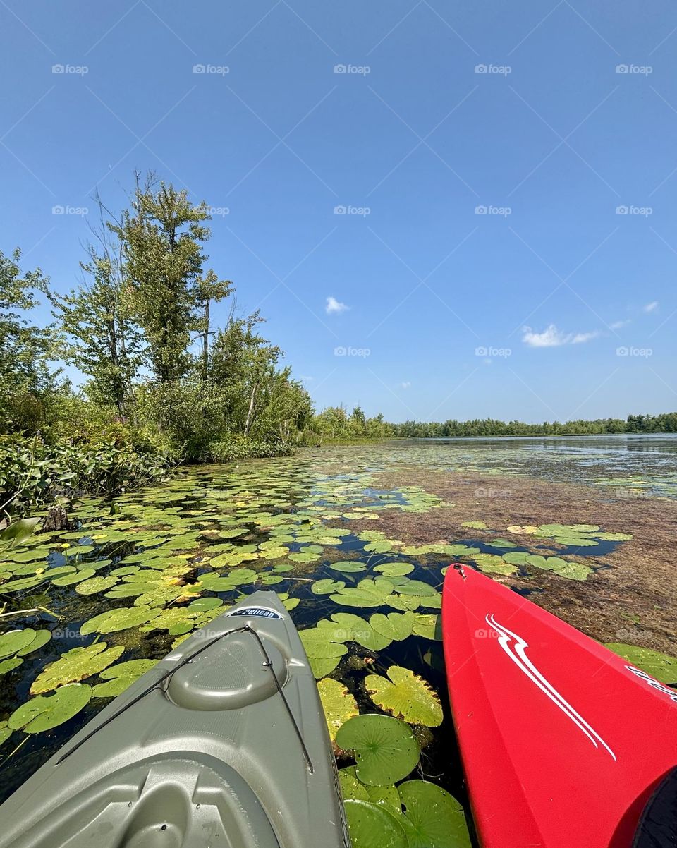 A pair of green and red kayaks on a lake on a sunny day.