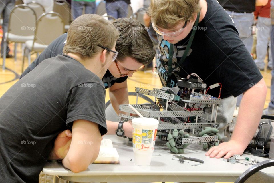 3 teenage boys working on a robot for a competition
