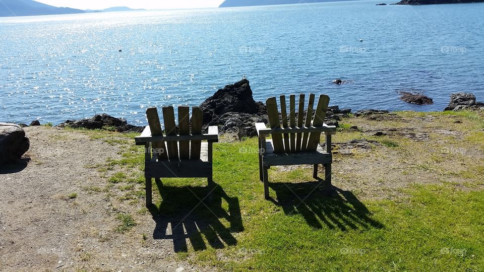 Empty chairs watching the sun's rays on the water