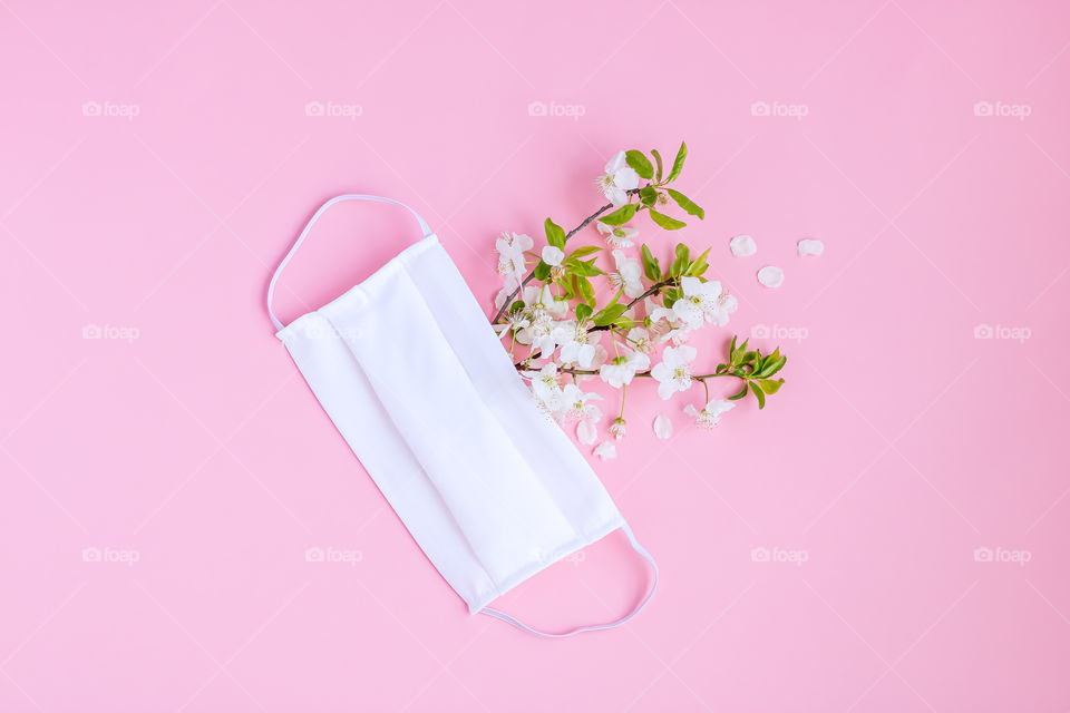 Abstract image of white protective mask and flowered branches on pink background. Concept of fight against of Covid-19.