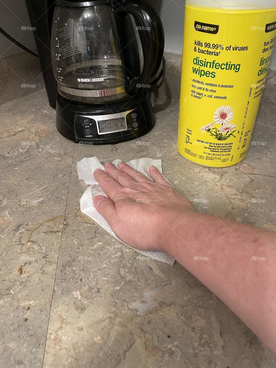 My cupboard cleaning done by No Name brand, disinfecting wipes in the yellow container, and showing my hand, fingers and arm wiping this counter off
