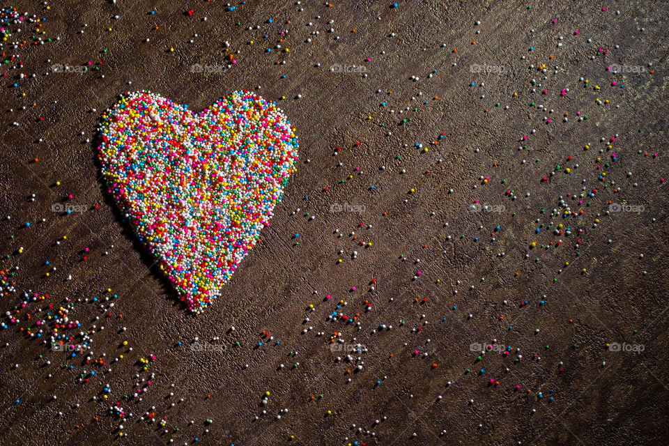 Heart shaped sugar sprinkles in different colors on a dark textured background