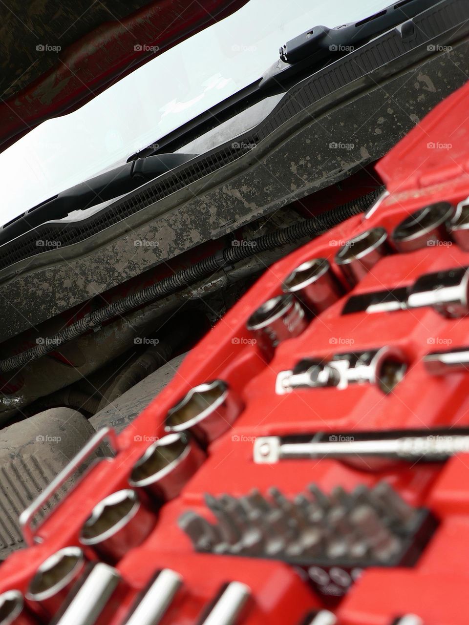 Under the hood of a red pickup truck with combination wrench set tools organized in a red tool hard case by the work station.