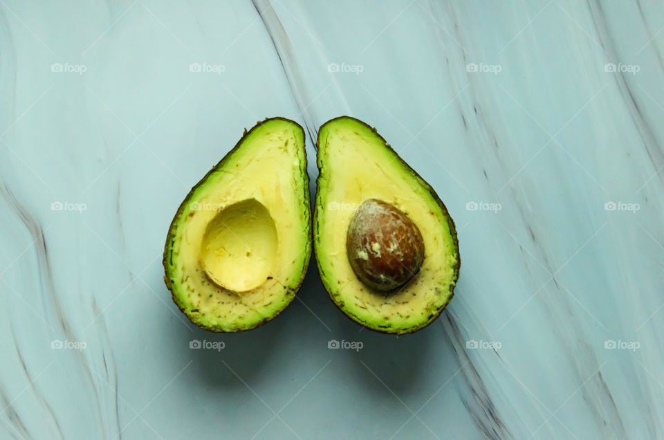 Two halves of avocado on a marble background. Cold shades. Top view.