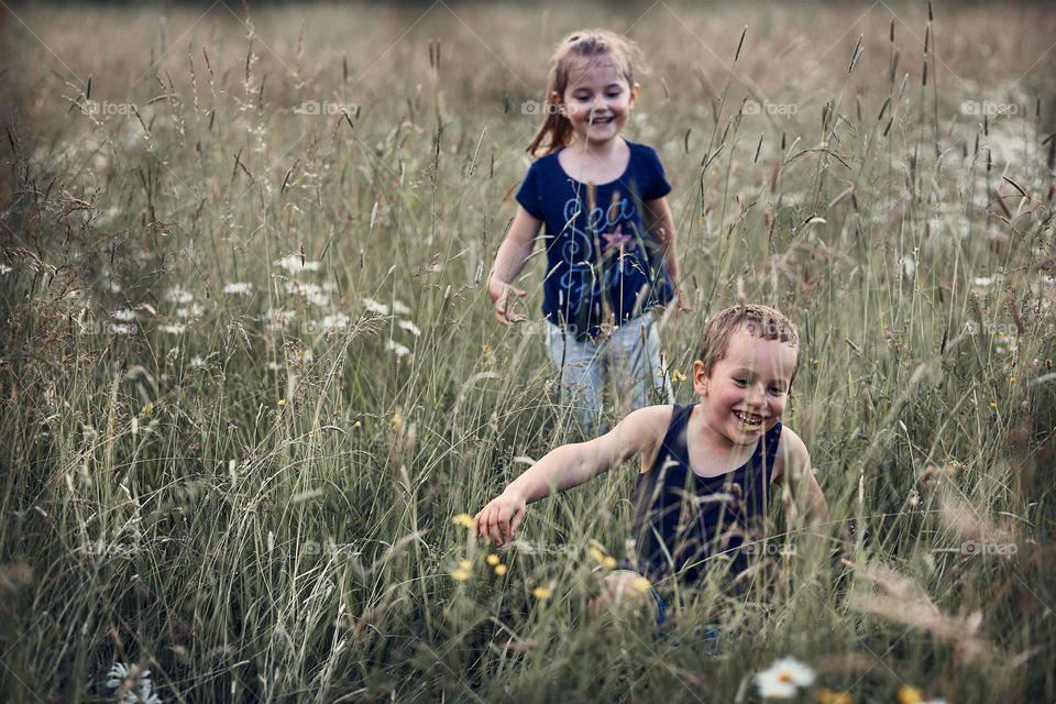 Little happy kids playing in a tall grass in the countryside. Candid people, real moments, authentic situations