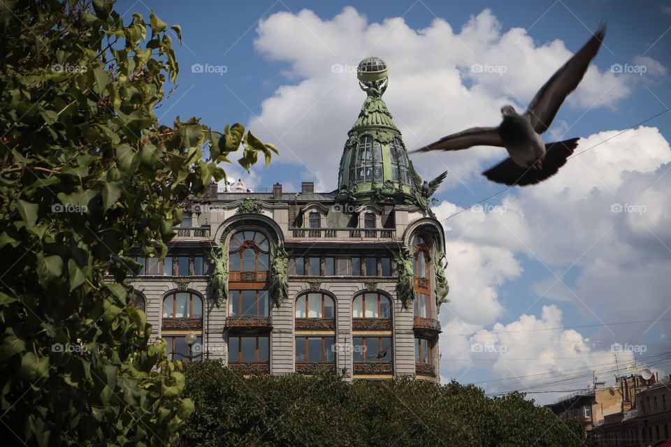 The Singer (Zinger) house, also known as the House of Books, on Nevsky avenue. dove in flight against the background of a beautiful building. blue sky, view of the house from green bushes