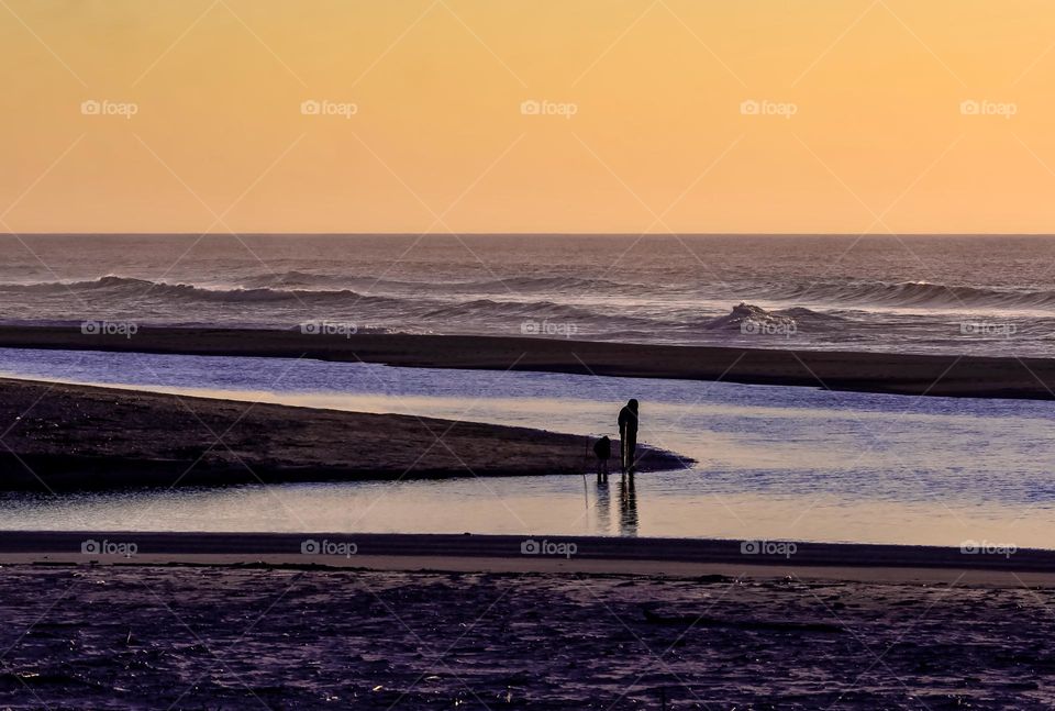 A parent & child on the beach just after sunset, exploring pools of water