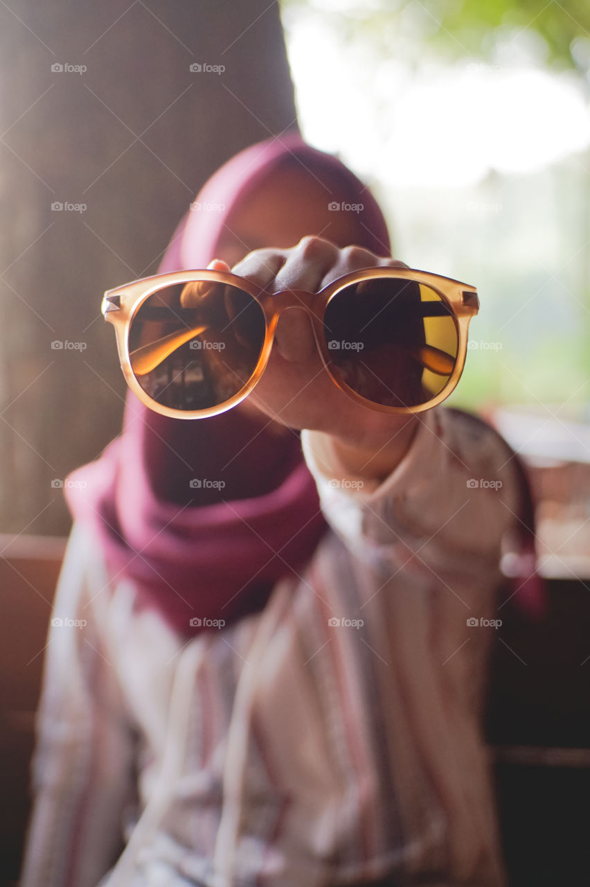 Woman wearing pink hijab holding brown glasses