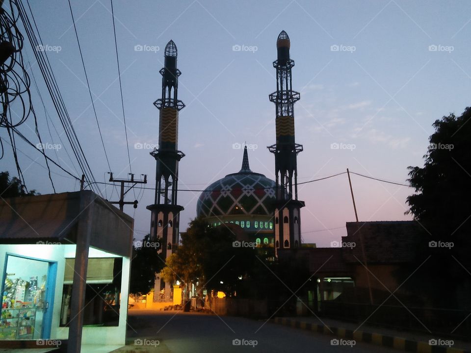 the photo of the mosque is light blue and has a golden yellow engraving and has two perfect-looking towers. if at night the mosque is glowing like sunside