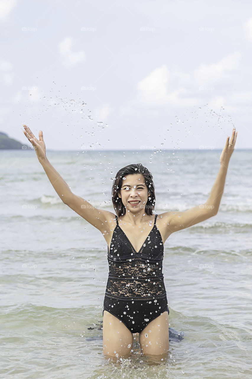 Portrait of Asian woman wearing a swimsuit play water in the sea.