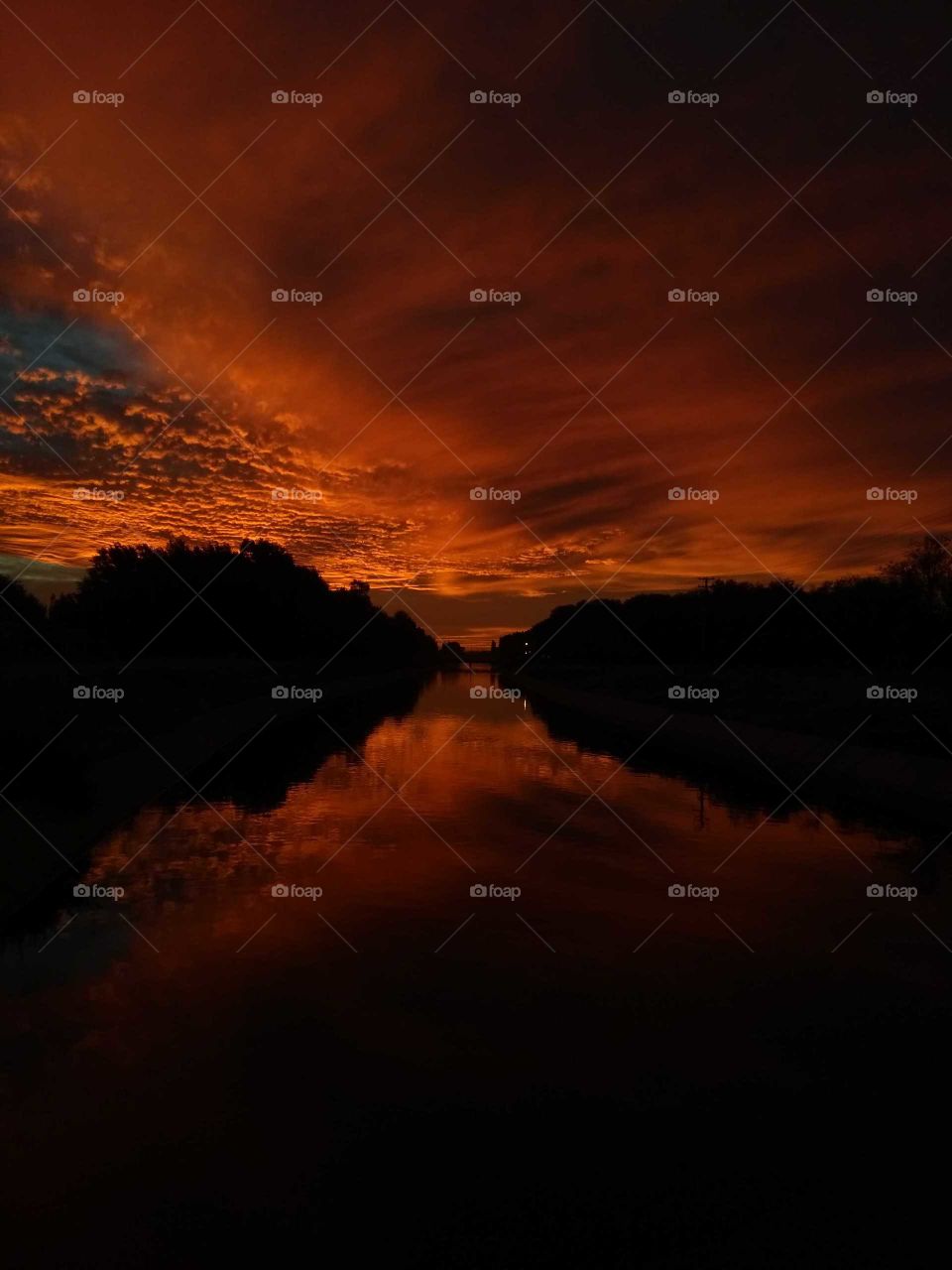 Atardecer otoñal anaranjado en un día nublado en canal de riego de la Ciudad de General Roca, Río Negro, Argentina