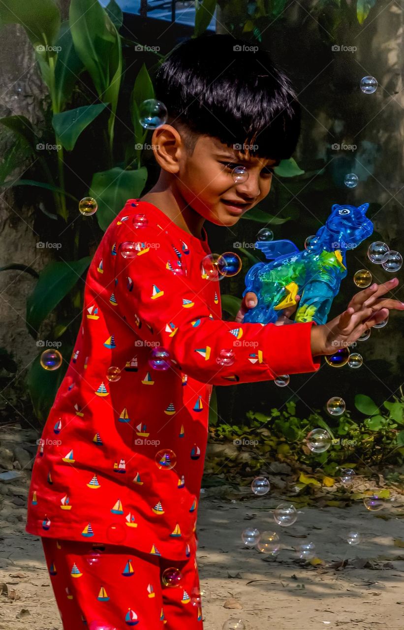 Boy playing with bubble gun wearing red dress