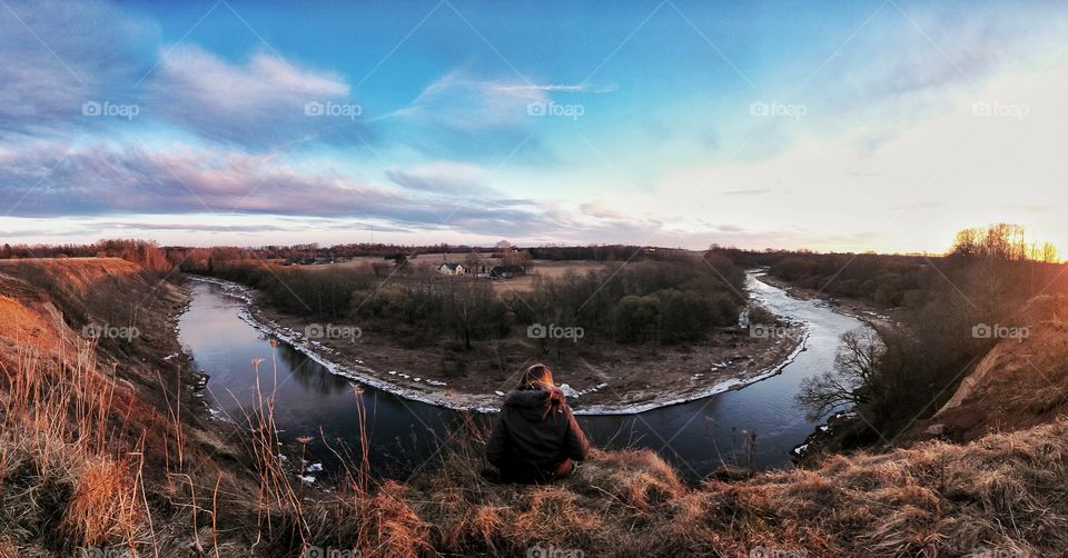 Girl sitting on the edge, watching sunset and listening for flowing river.